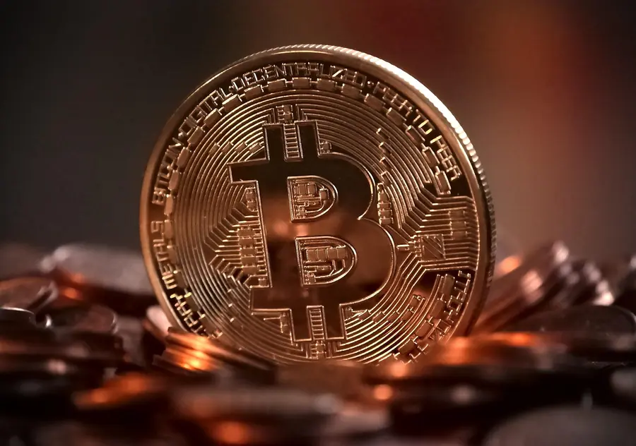 A physical Bitcoin coin resting on a pile of coins, illustrating cash-to-crypto conversion