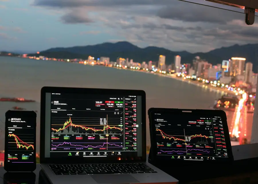 Laptops and tablets displaying crypto price charts against a city waterfront at dusk